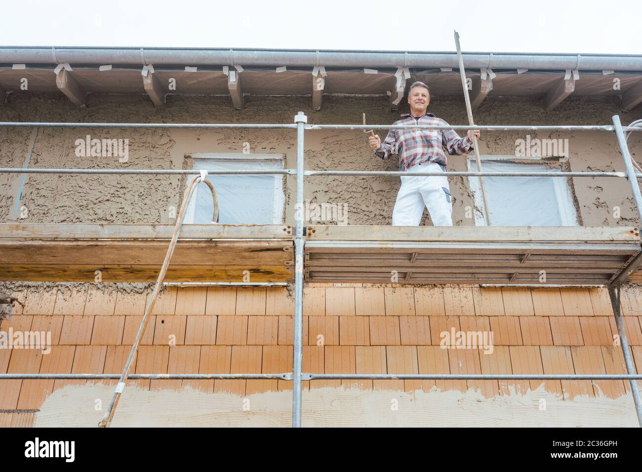 Gipser auf Gerüst auf der Baustelle mit Blick in die Kamera Stockfoto