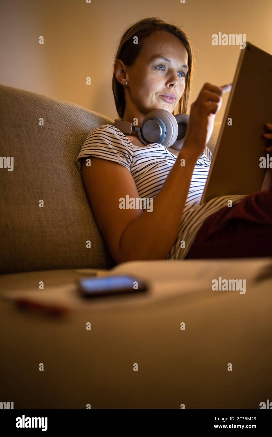 Hübsche, junge Frau, die zu Hause in den Abend arbeiten - mit Ihren Tablet-PC sowie Bluetooth® Kopfhörer, schreiben Sie einige Ideen für morgen Stockfoto