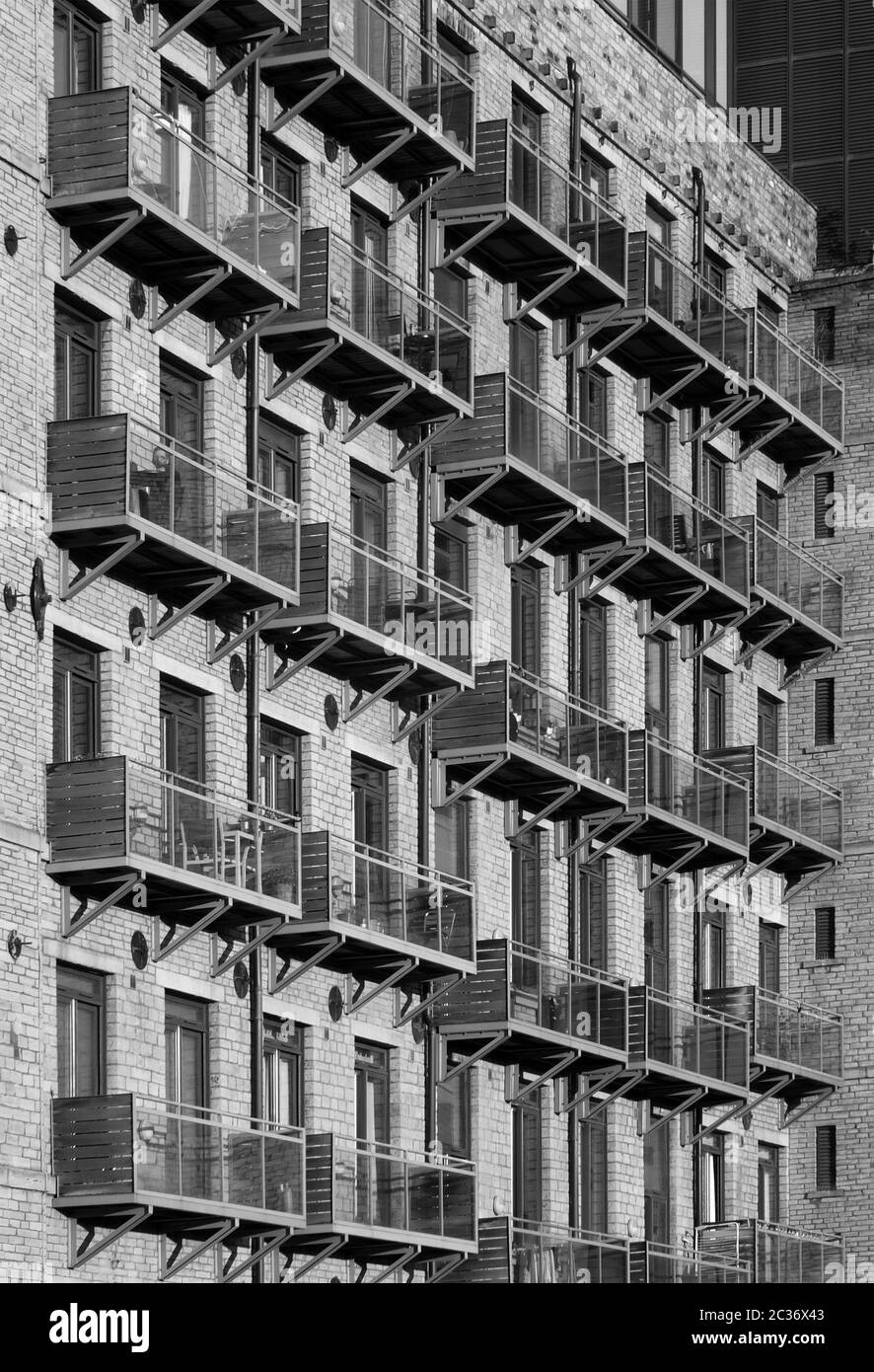 Ein monochromer perspektivischer Blick auf die Fassade eines großen alten Steinmühlengebäudes, das in Apartments mit modernem Glasbalco umgewandelt wurde Stockfoto