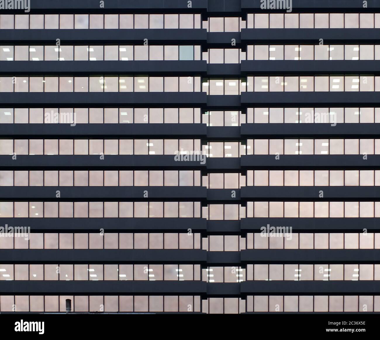 Die Fassade eines großen städtischen Bürogebäudes mit Reihen von Fenstern, die bei Dämmerung beleuchtet werden Stockfoto