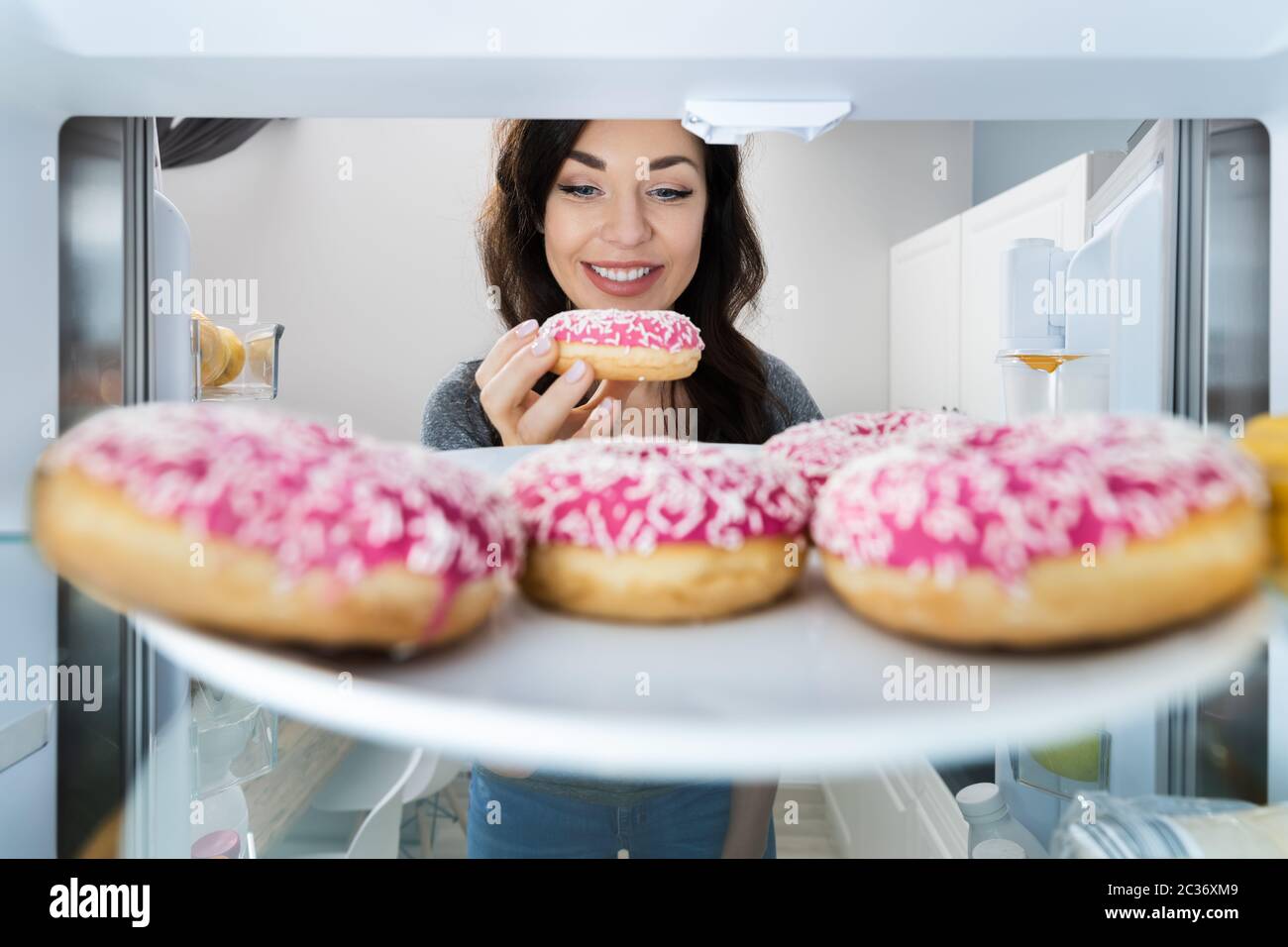 Happy Young Woman Einnahme Donut Aus Kühlschrank Oder Gefrierschrank Stockfoto