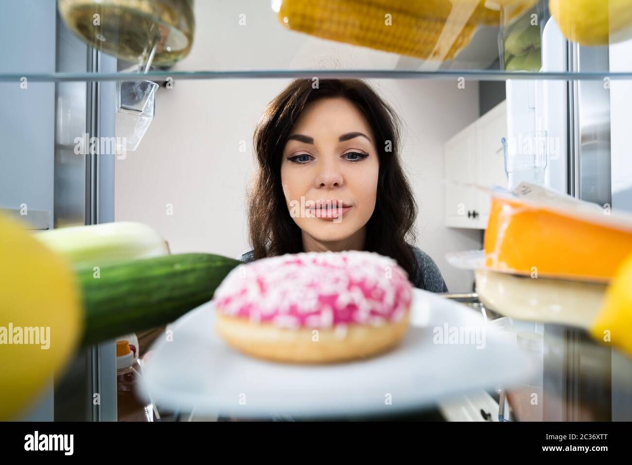 Glückliche Junge Frau, Die Donut Aus Dem Kühlschrank Oder Gefrierschrank Betrachtet Stockfoto