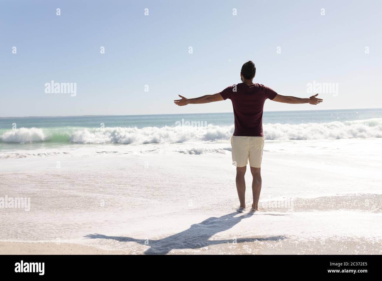 Junger Mann mit gemischter Rasse, der am Strand die Arme hebt Stockfoto