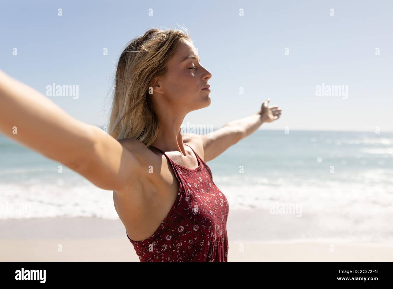 Junge kaukasische Frau, die am Strand die Arme hebt Stockfoto