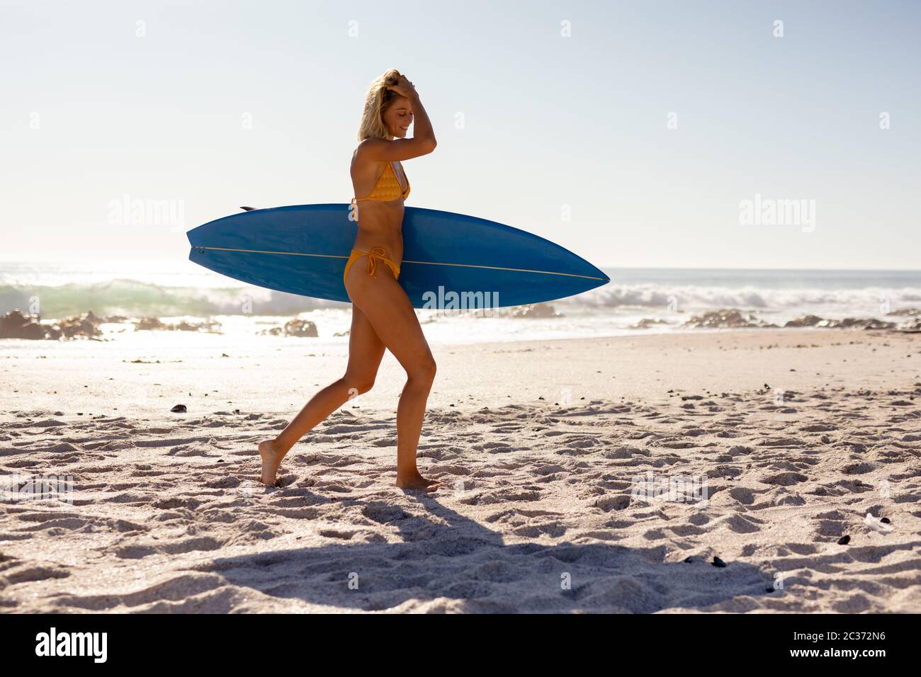 Junge kaukasische Frau hält Surfbrett am Strand Stockfoto