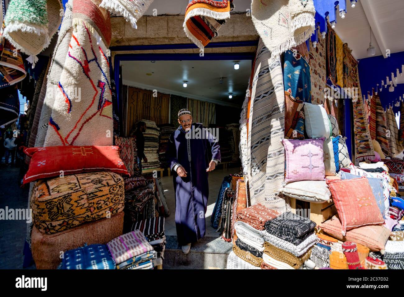 Essaouira, Marokko, 2019. Februar: Mann Verkäufer marokkanischen handgefertigten Textilien, Teppiche und Teppiche auf dem Straßenmarkt. Marokkanische Altstadt Medina mit Geschäften Stockfoto