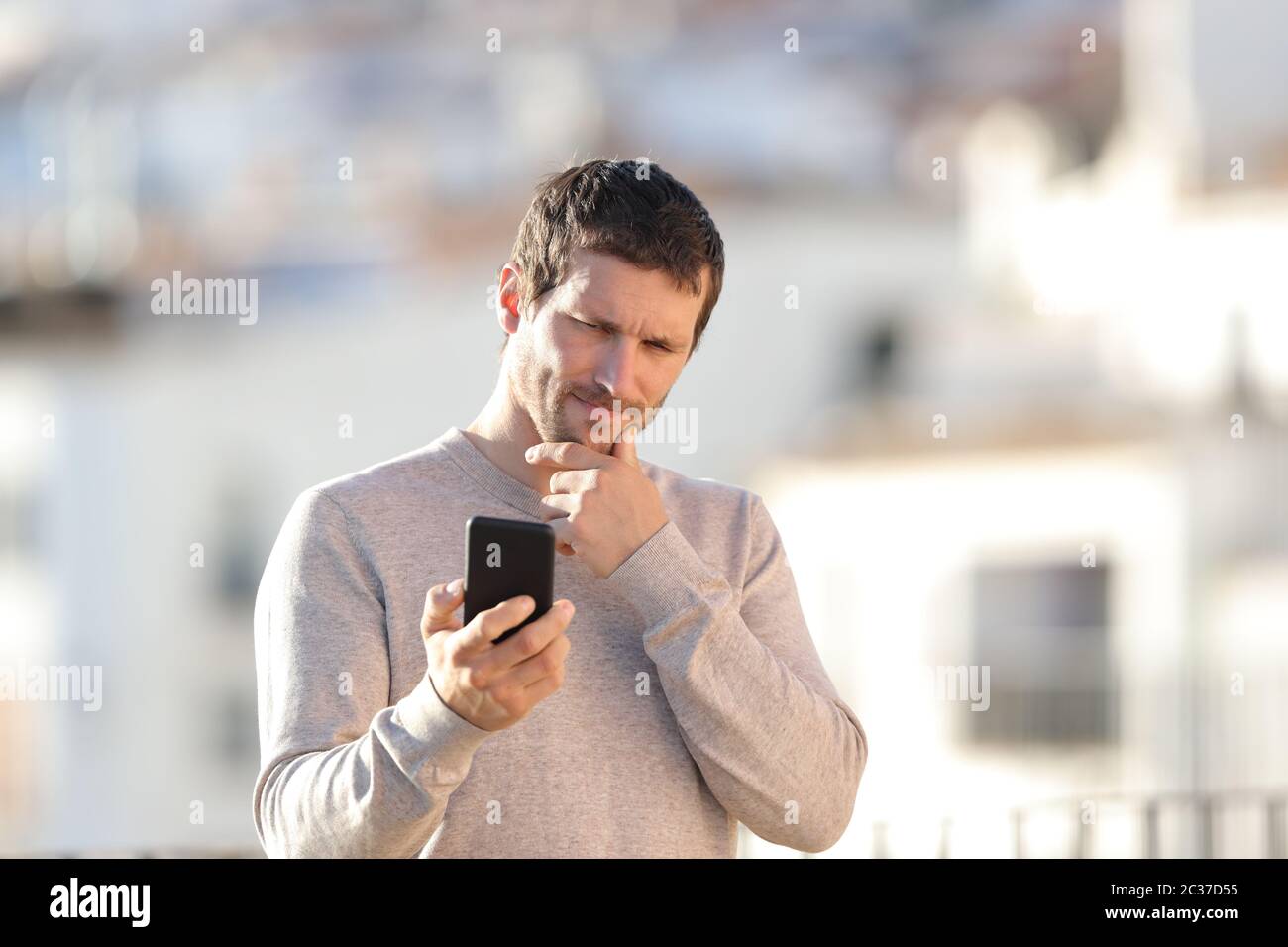 Zweifelnd erwachsenen Mann Kontrolle smart phone Inhalt in einer ländlichen Stadt Stockfoto