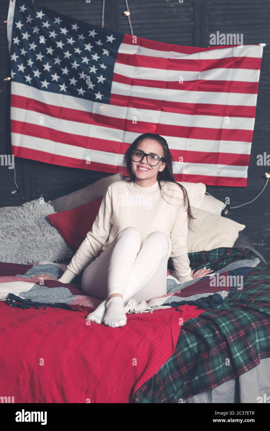 Hübsche Hündin in Casualwear auf dem Bett mit amerikanischer Flagge an der Wand Stockfoto