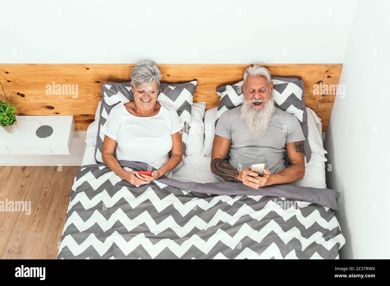Happy Senior paar mit mobilen Smartphones unter Decken im Bett - ältere Menschen mit lustigen Bett Zeit beobachten auf neue Medien Trends Stockfoto
