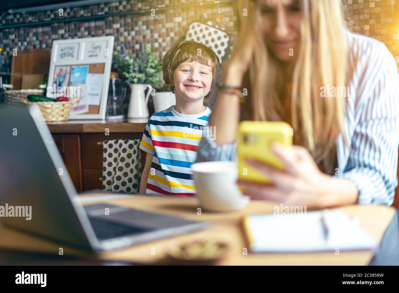 Mutter arbeitet von zu Hause und Online-Bildung mit Kind. Gestresst mit Computer und Telefon. Kind machen Lärm und stören Frau bei der Arbeit. Heimschooling Stockfoto