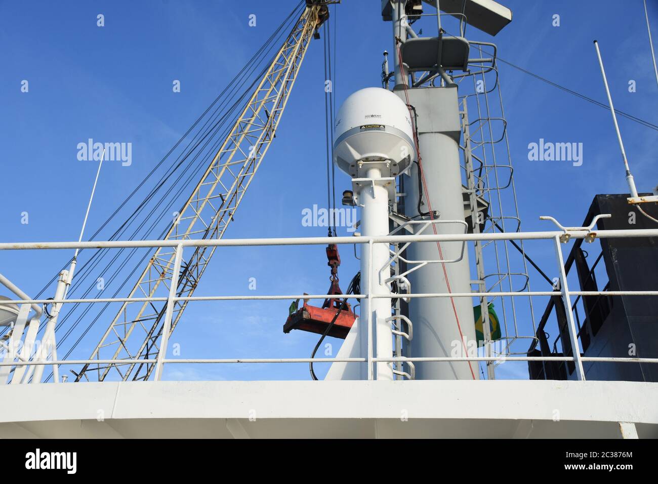 Satellitenantenne mit Radarmast des Handelsschiffes mit dem Ladekran im Hintergrund während des Frachtbetriebs beim Schiff im Hafen Stockfoto