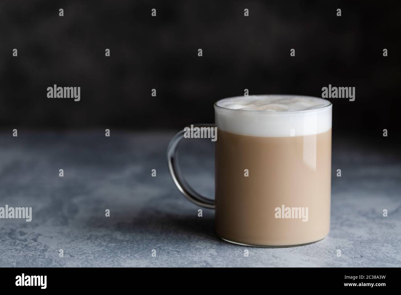 Eine Tasse Kaffee Latte, Cafe au lait oder Chai Latte. Das Foto zeigt ein beiges oder hellbraunes Getränk mit einem weißen Schaum auf dem Dach. Das Getränk ist in einem Glas Becher wi Stockfoto