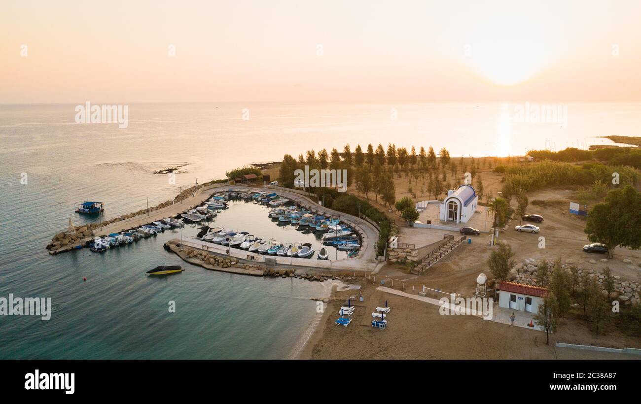 Luftbild des Sonnenuntergangs an der Küste und die weiße, gewaschene Kapelle am Strand Agia Triada, Protaras, Famagusta, Zypern von oben. Vogelperspektive auf Tour Stockfoto