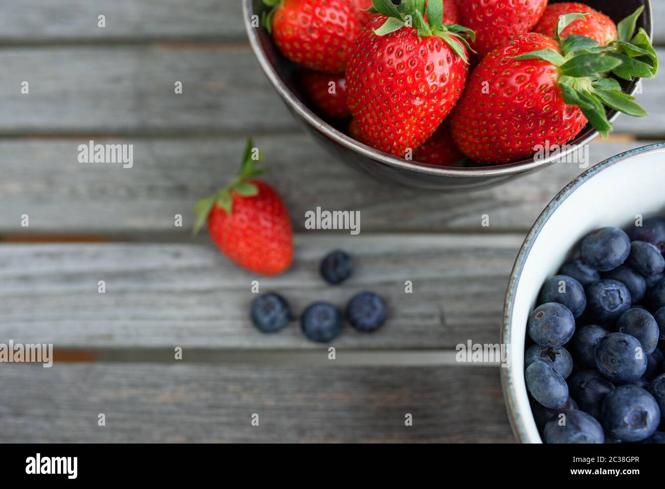 Frische Erdbeeren und Heidelbeeren in einer Schüssel auf grauen Holzbohlen. Hintergrund mit kurzen Tiefenbereich für eine gesunde Ernährung und Lebensstil. Draufsicht. Stockfoto