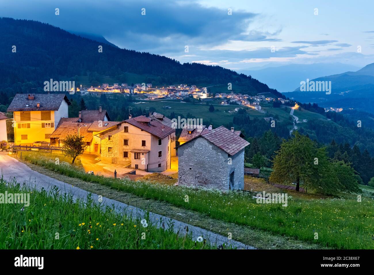Im Dorf Perpruneri auf der Alpe Cimbra fällt die Nacht. Im Hintergrund das Dorf San Sebastiano. Folgaria, Trentino, Italien. Stockfoto