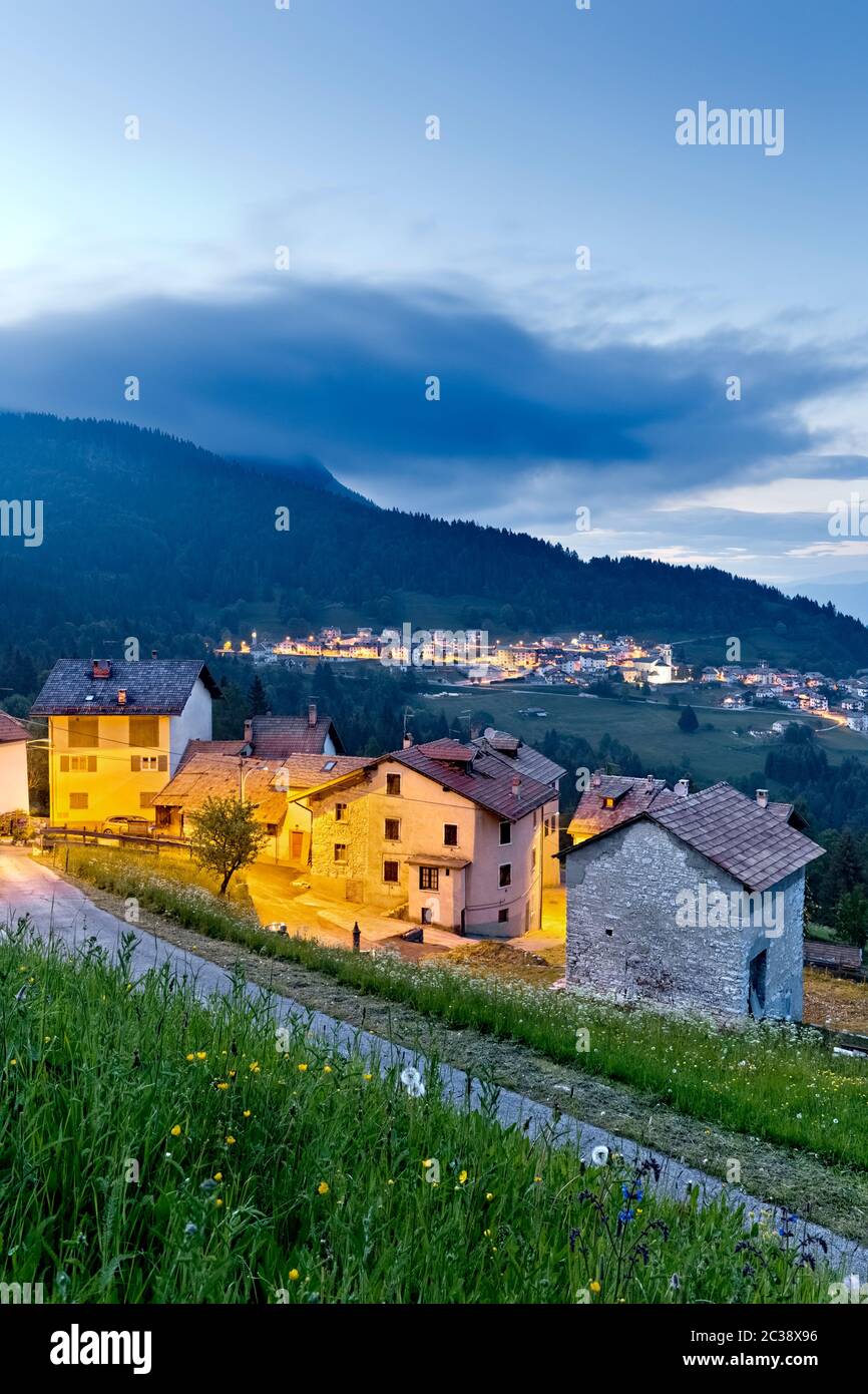 Im Dorf Perpruneri auf der Alpe Cimbra fällt die Nacht. Im Hintergrund das Dorf San Sebastiano. Folgaria, Trentino, Italien. Stockfoto