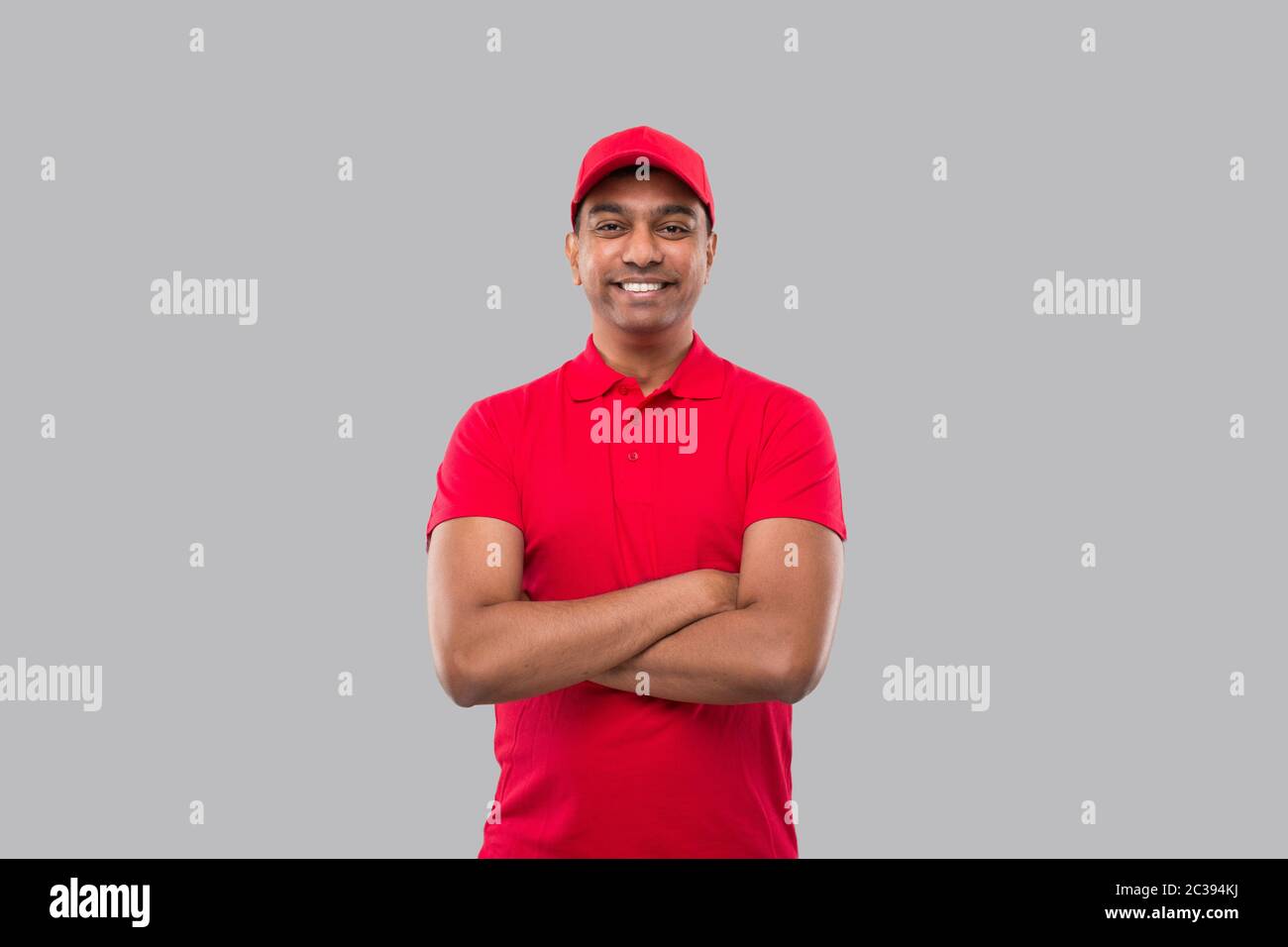 Delivery Man Stehende Hände Kreuzten Lächelnd. Indische Lieferung Junge in rot Uniform isoliert Stockfoto