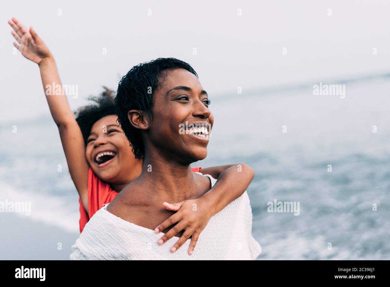 Schwarze Mutter und Tochter laufen am Strand bei Sonnenuntergang Zeit während der Sommerferien - Familie Leute, die Spaß zusammen im Freien - Reisen und happines Stockfoto