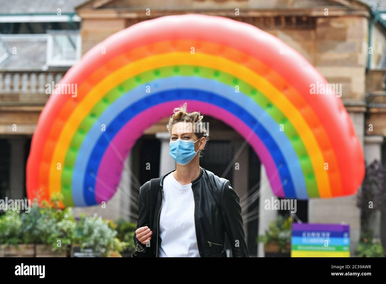 Eine Frau mit Gesichtsmast geht in Covent Garden, London, an einem großen Regenbogen vorbei, nachdem die britischen Chefs vereinbart hatten, die Alarmstufe des Coronavirus von vier auf drei herabzustufen, nachdem die Fälle in allen vier Nationen „stillstehen“ und weiterhin zurückgehen. Stockfoto