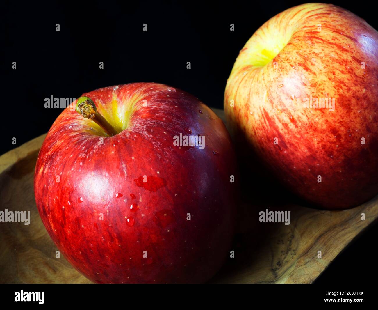 Zwei gewaschene braeburn Äpfel mit Wassertropfen in einer Holzschale vor schwarzem Hintergrund Stockfoto