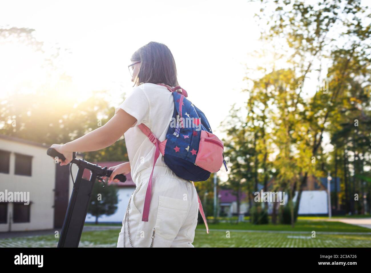 Ziemlich junge Studentin in Brillen Reiten blauen Elektro-Kick Scooter im Park Stockfoto