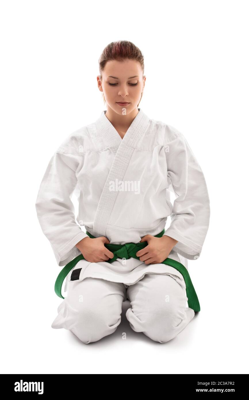 Schöne weibliche Kampfkunstkämpferin in einem weißen Kimono mit grünem Gürtel in der Seiza-Position, nach unten schauend, isoliert auf weißem Hintergrund. Ruhig jung g Stockfoto