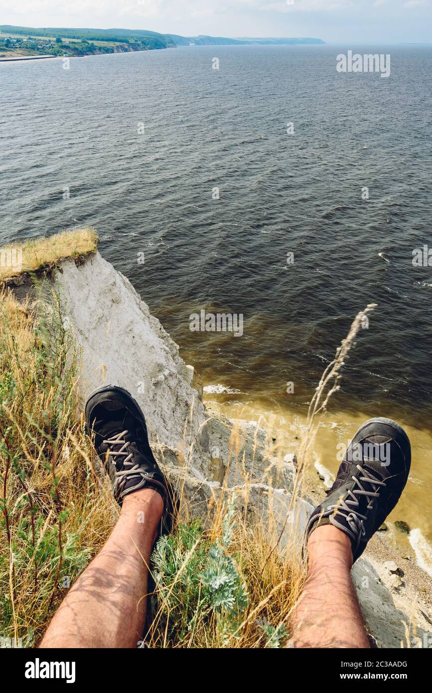 POV-Sicht der Mann sitzt auf dem Rand der Klippe mit Blick auf den Fluss Stockfoto