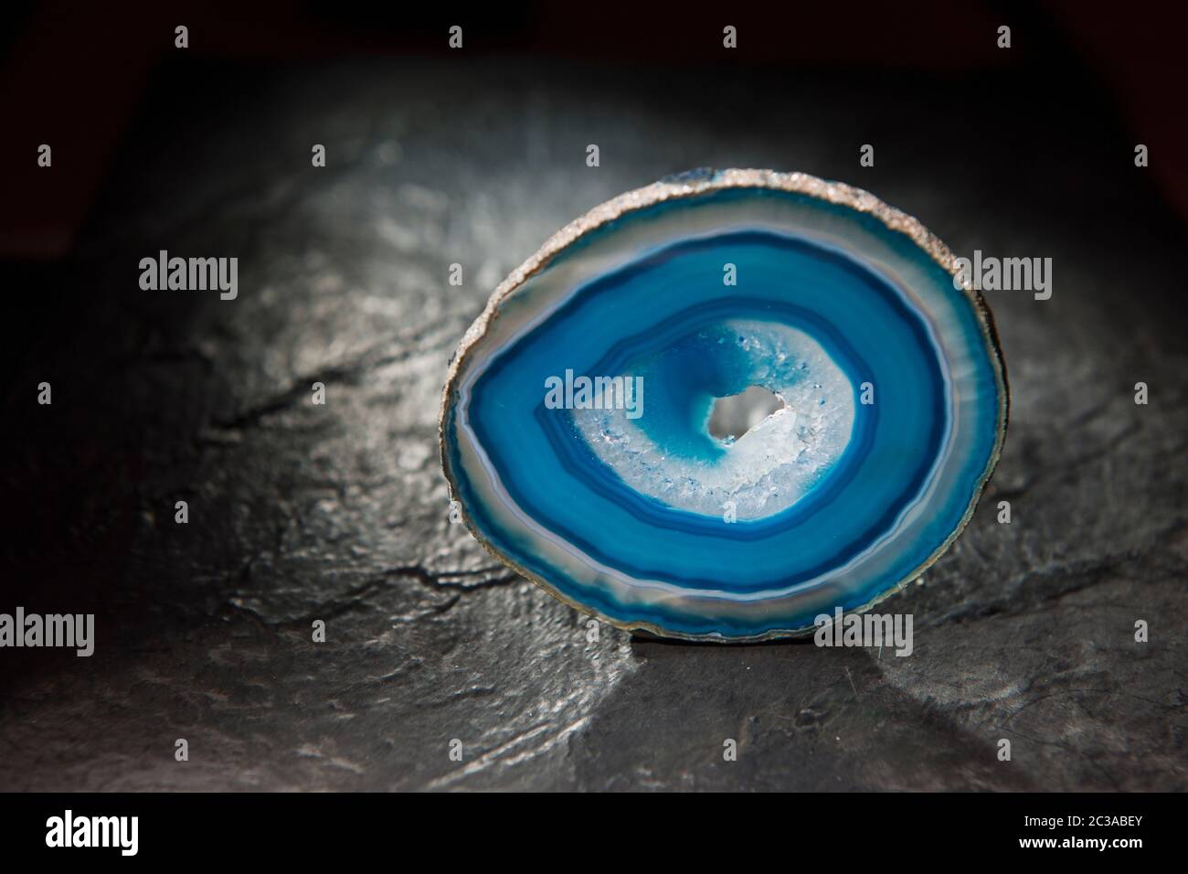 Studio-Aufnahme einer dünnen, polierten Scheibe eines runden Achats mit blauen kreisförmigen gebänderten Körnung und mittlerer Druse (Loch) umgeben von kristallinen Strukturen sta Stockfoto