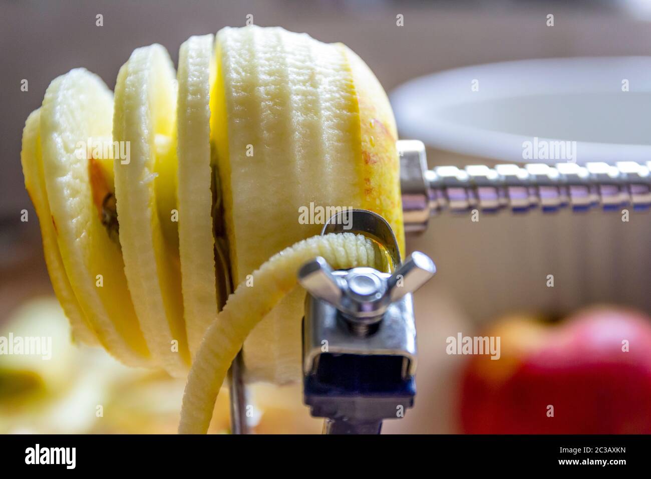 Ein Apfel wird auf einem Apple Slicer geschnitten und geschält, mit einer Schüssel und Äpfel im Hintergrund Stockfoto