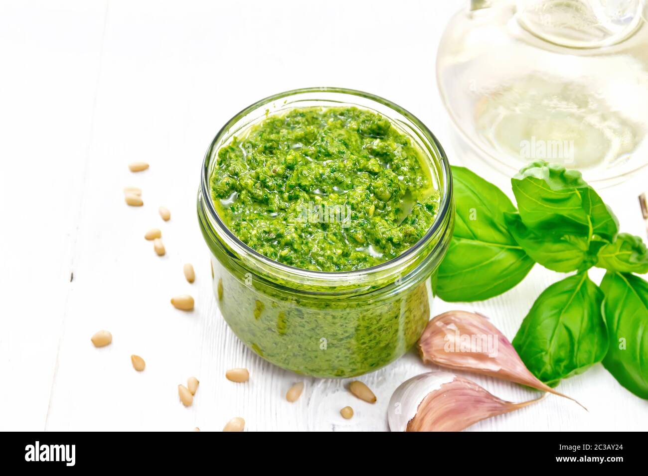 Pesto in einem Glas, Pinienkerne, Knoblauch, Basilikum und Olivenöl in eine Karaffe auf Holzbrett Hintergrund Stockfoto