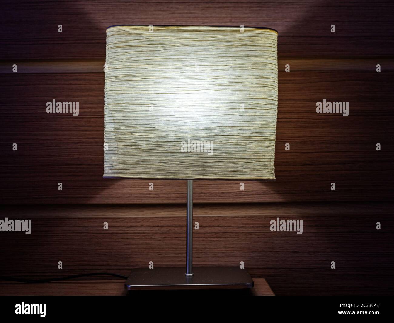 Nachttischlampe leuchtet auf dem Hintergrund einer braunen Holzwand Stockfoto