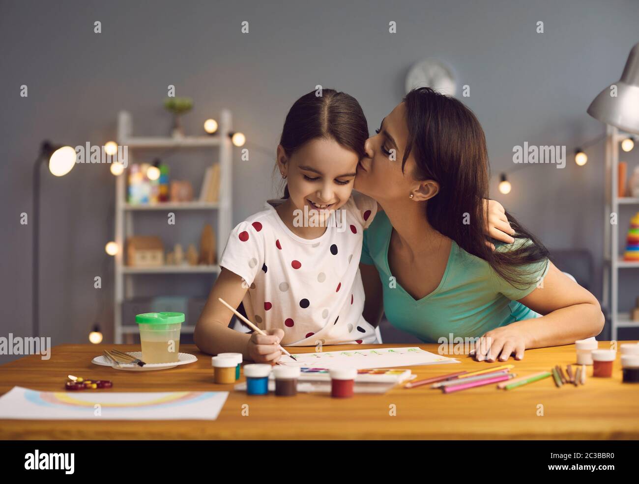Das Kind zeichnet eine Zeichnung. Mutter lehrt Tochter, mit Farben auf Papier zu zeichnen, die an einem Tisch im Wohnzimmer sitzen. Stockfoto