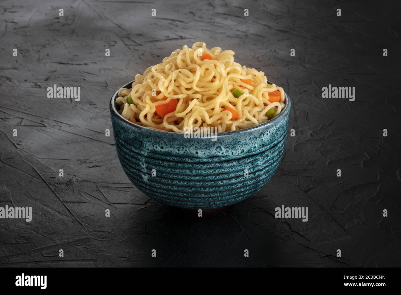 Instantnudeln mit Karotten und Hengsten, eine Schüssel Soba mit Gemüse auf schwarzem Hintergrund Stockfoto