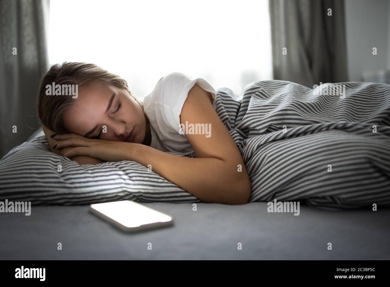 Hübsche, junge Frau, die in ihrem Bett mit ihrem Handy in ihrer Nähe schläft. Smartphone On Bed Mobile Addict Konzept. Stockfoto