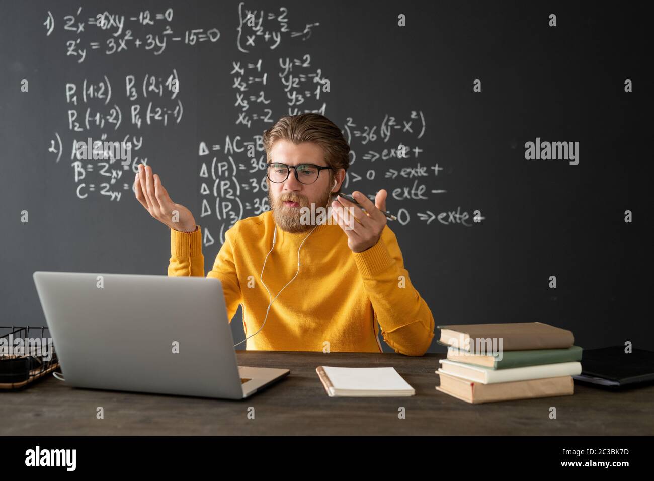 Selbstbewusster Lehrer in Brillen, der sein Publikum auf dem Laptop-Display ansieht und während des Online-Unterrichts neue Formel auf der Tafel erklärt Stockfoto