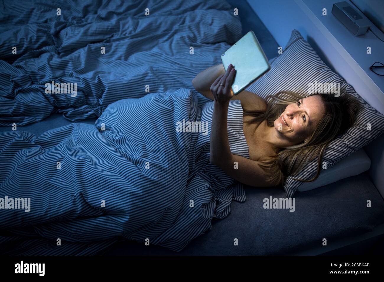 Hübsche Frau mittleren Alters mit Ihrem Tablet-PC vor dem Schlafen im Bett am Abend Stockfoto
