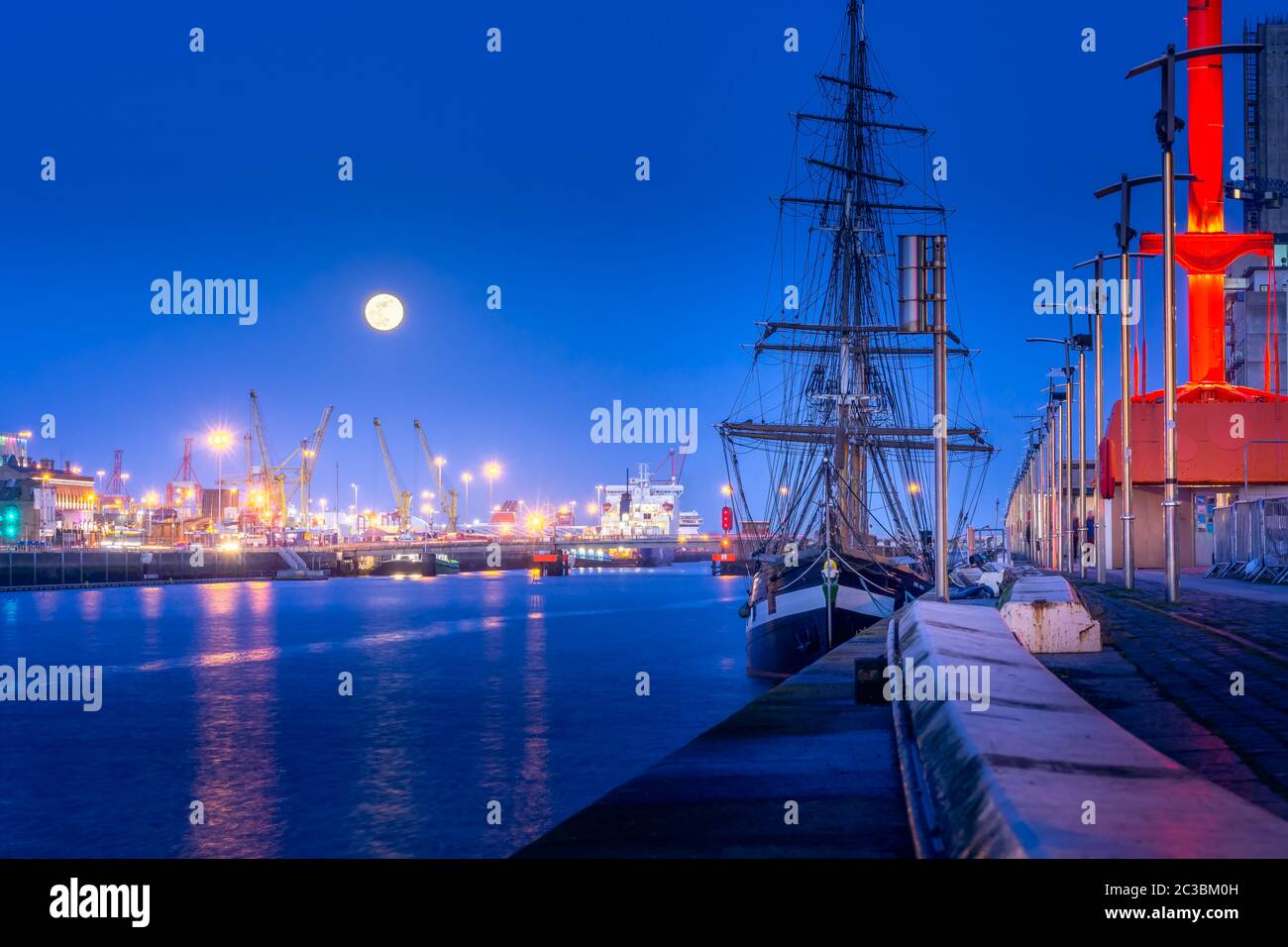 Tall Ship angedockt in Dublin Dock auf Liffey River, Blaue Stunde und Vollmond. Beleuchtete Embankment und fließend Wasser, Fotos mit langer Belichtungszeit, Irland Stockfoto
