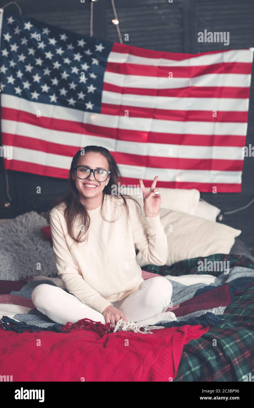 Hübsche Hündin in Casualwear auf dem Bett mit amerikanischer Flagge an der Wand Stockfoto