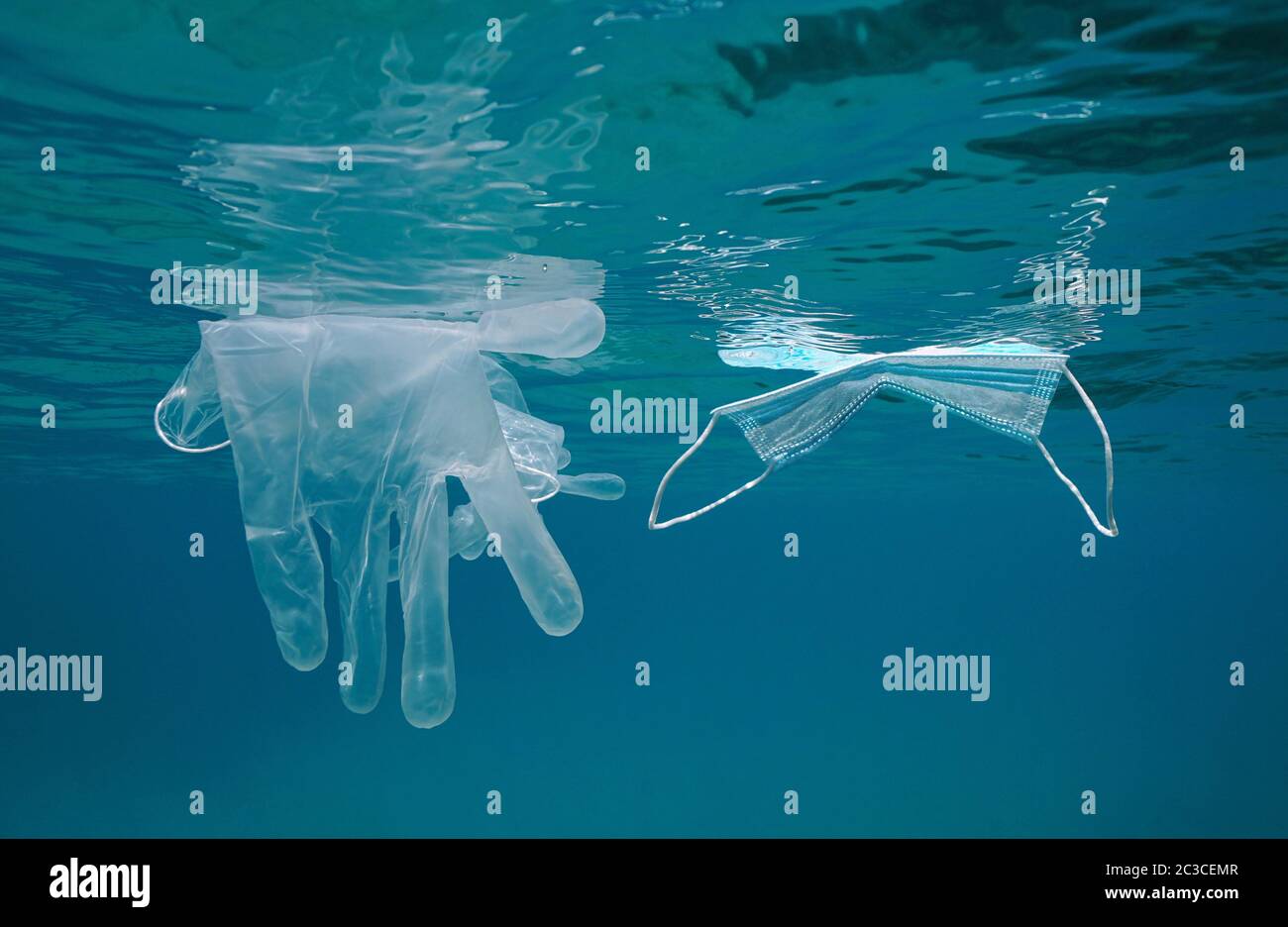 Gesichtsmaske und Handschuhe schwimmen unter der Wasseroberfläche im Meer, Plastikmüll Verschmutzung seit Coronavirus COVID-19 Pandemie Stockfoto