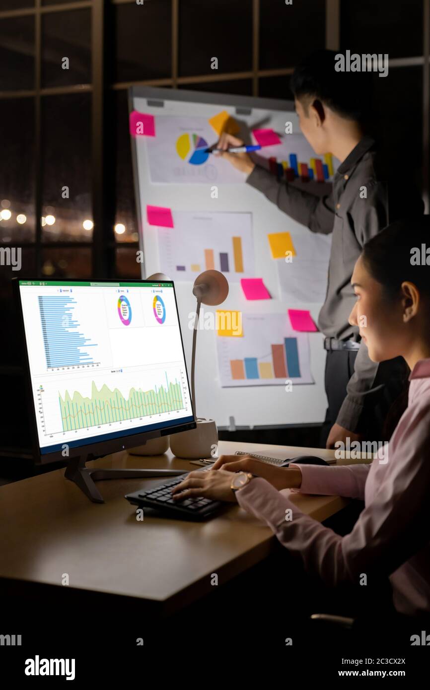 Junge Erwachsene asiatische Unternehmer diskutieren mit Kollegen über die Arbeit mit der Analyse Grafik auf dem Whiteboard spät in der Nacht in ihrem Büro mit Computer. Stockfoto