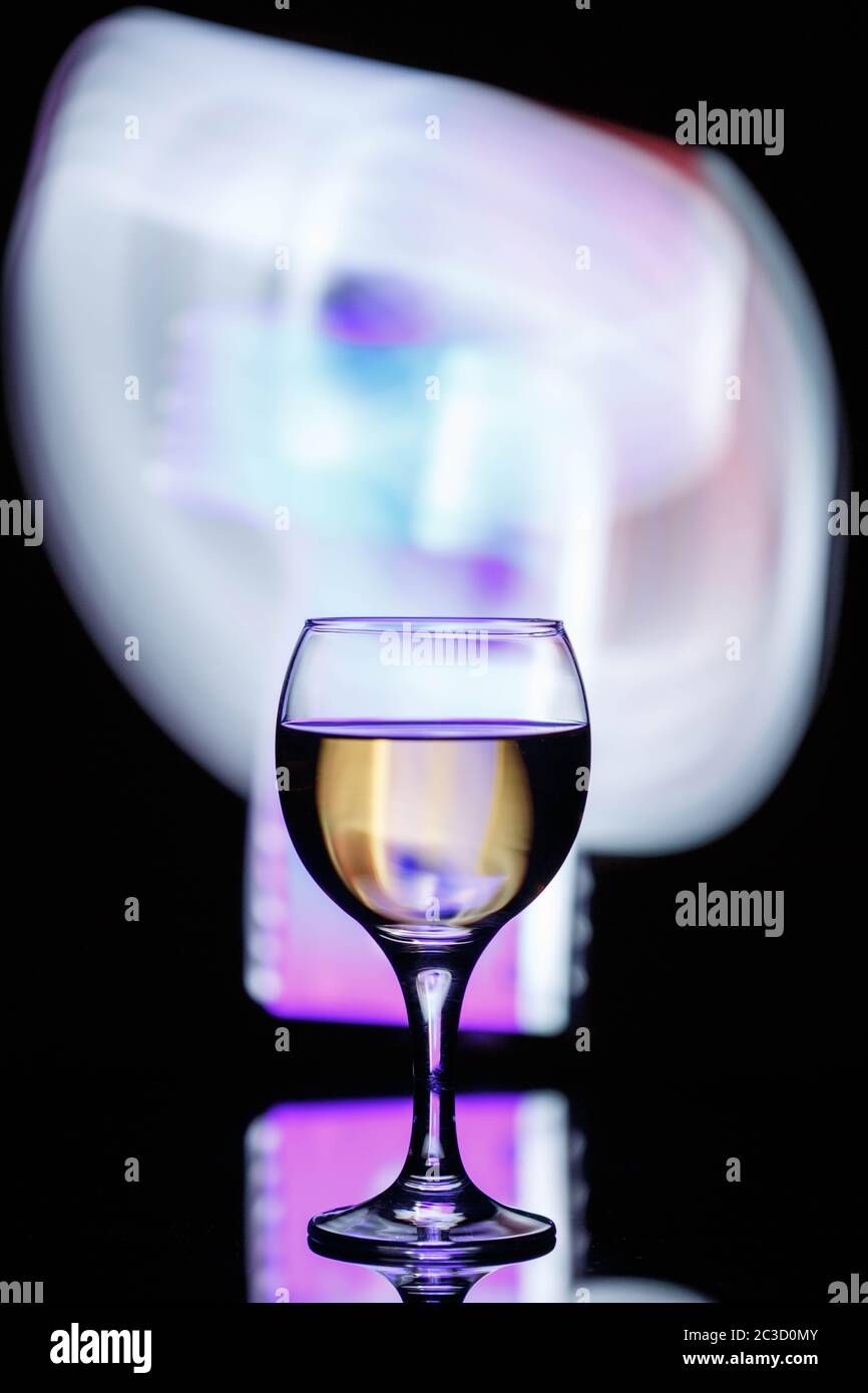 Ein Glas mit einem Drink auf einem dunklen schönen Hintergrund mit farbigem Licht beleuchtet. Stockfoto