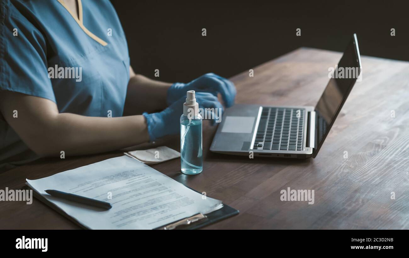 Seitenansicht der Ärztin mit Computer am Schreibtisch mit medizinischen Rohling und antiseptischen Spray auf sie sitzen. Nahaufnahme. Getöntes Bild Stockfoto