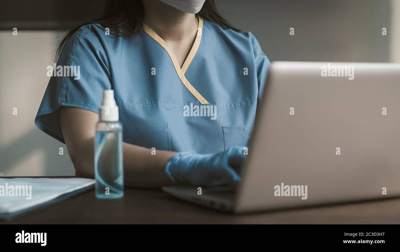 Vorderansicht der Krankenschwester oder des Arztes mit Laptop. Frau in blauer medizinischer Arbeitskleidung, die auf der Computertastatur tippt. Nahaufnahme. Getöntes Bild Stockfoto
