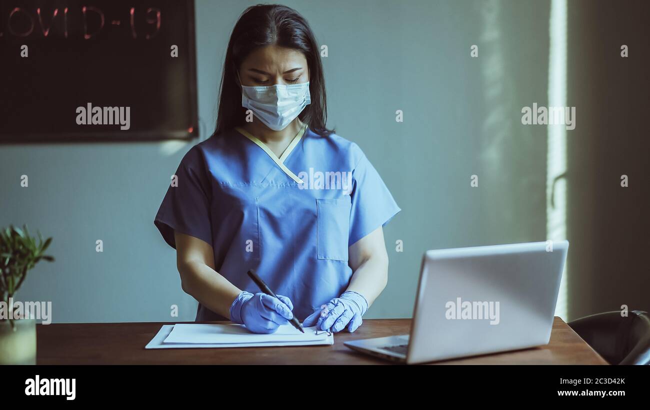 Ziemlich asiatische Krankenschwester oder Arzt schreibt auf medizinischen leer stehend neben Tisch mit Laptop-Computer auf sie. Medizinkonzept. Getöntes Bild Stockfoto