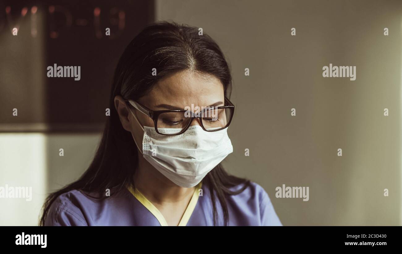 Porträt einer schweren müden Frau in Schutzmaske und Brillen Blick nach unten. Arzt mit Laptop in ihrem Büro. Nahaufnahme. Getöntes Bild Stockfoto
