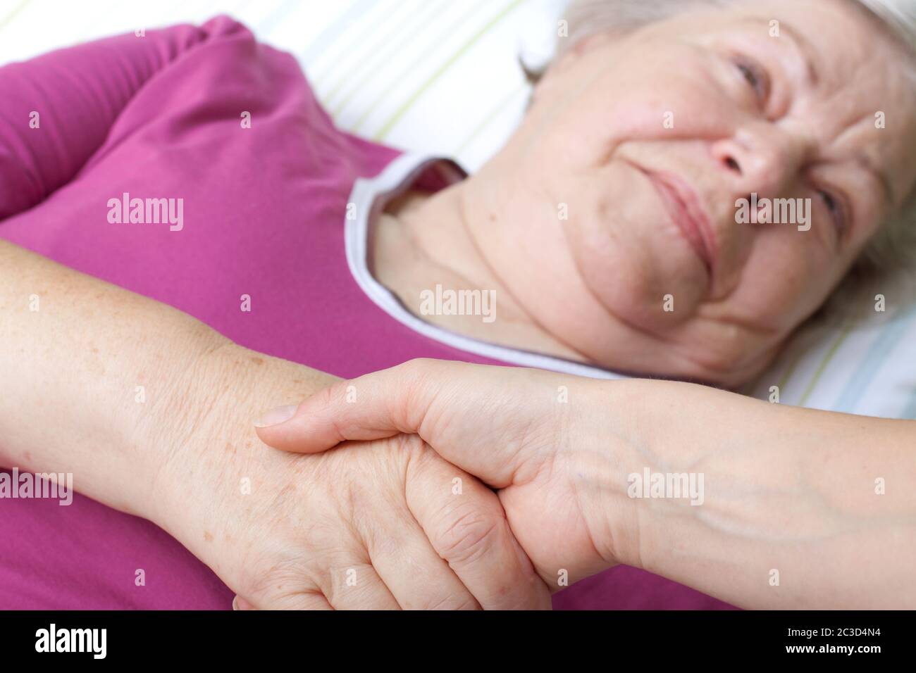 Ältere Frau liegt im Bett und begrüßt die Krankenschwester Stockfoto