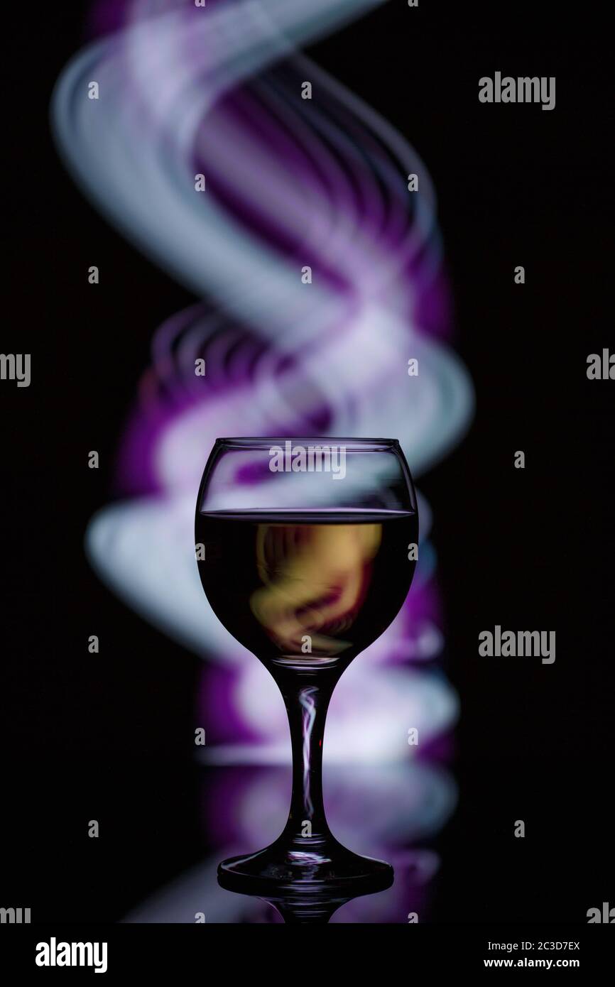 Ein Glas mit einem Drink auf einem dunklen schönen Hintergrund mit farbigem Licht beleuchtet. Stockfoto