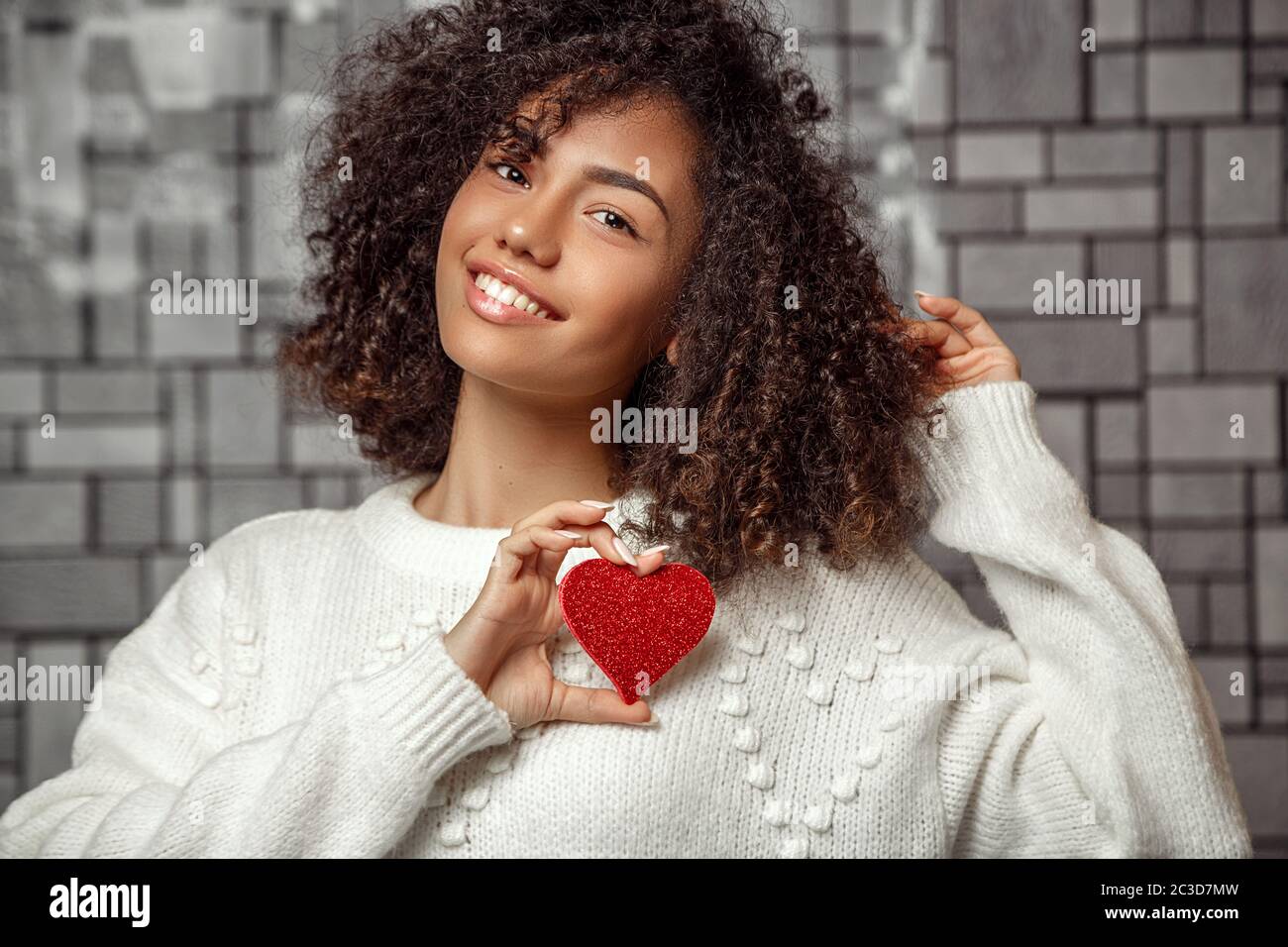Nahaufnahme Porträt eines jungen lockigen afroamerikanischen Mädchen in einem weißen Pullover mit einem Papier Herz. Flache Tiefe des FOC Stockfoto