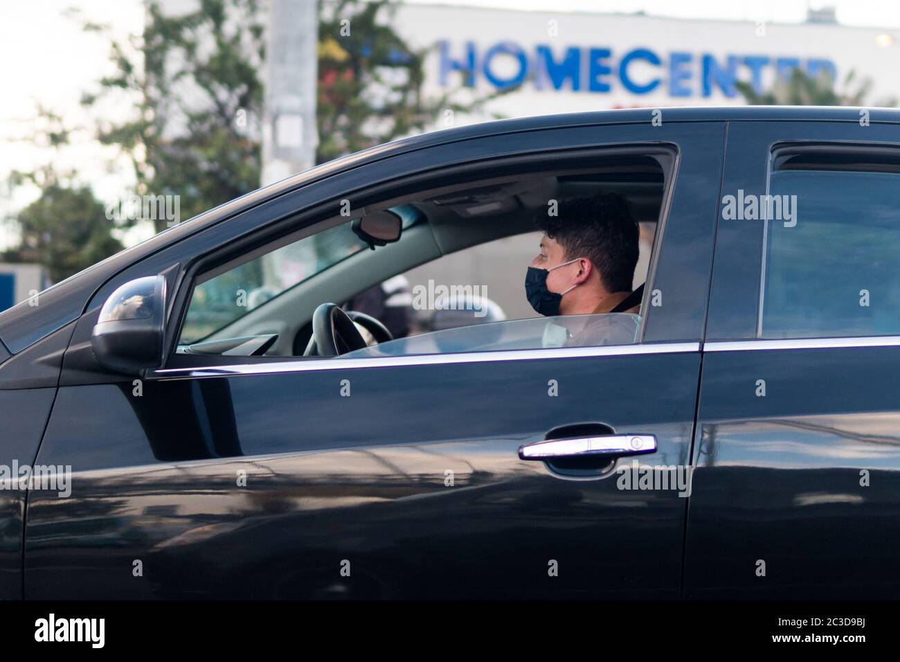 Junger Latein, der eine Maske trägt, um die Ausbreitung des Coronavirus zu vermeiden; fährt sein schwarzes Auto auf den Straßen von Bogota. Kolumbien. Heimzentrum Lager hinter Stockfoto