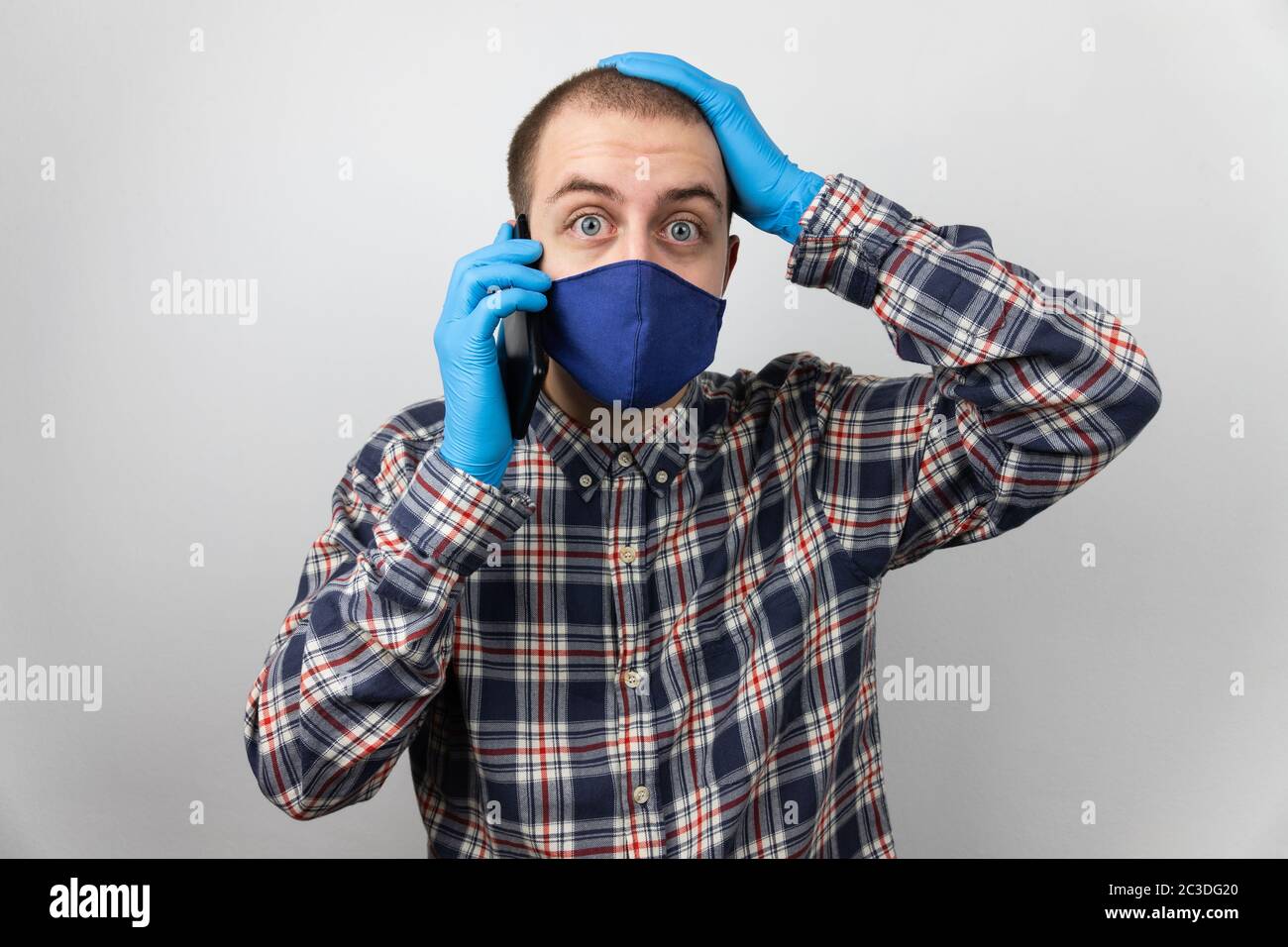 Mann, der am Telefon sprach, erhielt sehr schlechte und traurige Nachrichten, beunruhigte Ausdruck, trägt blaue Schutzhandschuhe und Gesichtsmaske auf seinem Kinn. Auf weißem Hintergrund Stockfoto